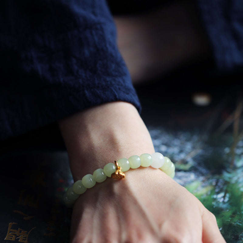Jade Lotus Abundance Bracelet – Worn on wrist with gold lotus charm, moody blue water background, jade wristlet