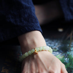 Jade Lotus Abundance Bracelet – Worn on wrist with gold lotus charm, moody blue water background, jade wristlet