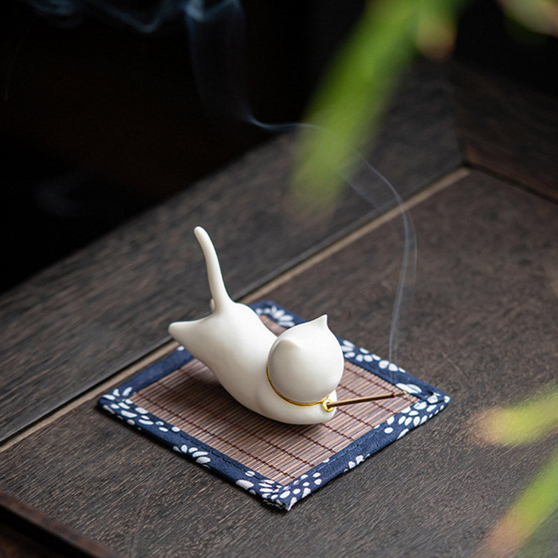 Cream ceramic cat incense holder with gold collar, incense smoke on blue mat