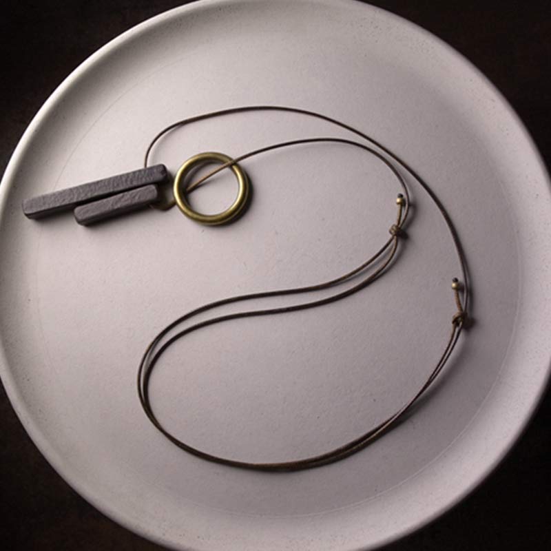 Zen Circle Ebony Wood Necklace - adjustable cord with black bar and brass ring on white plate, artisan craft