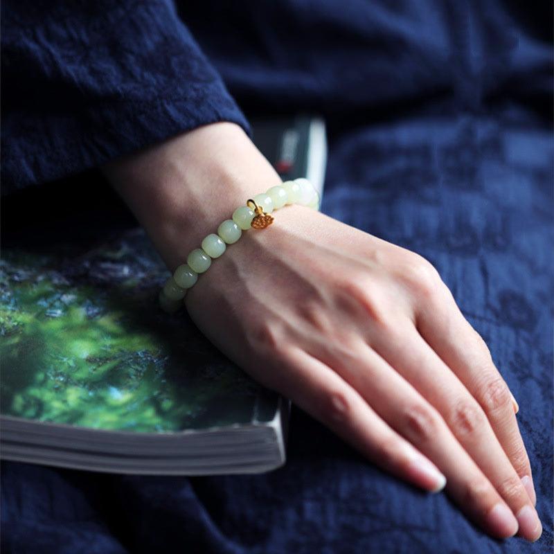 Jade Lotus Abundance Bracelet – Worn on wrist resting on book, navy fabric, lotus jade wrist jewelry