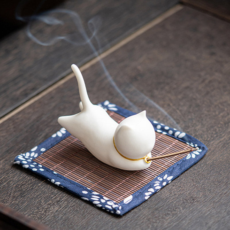 White ceramic cat incense holder in stretch pose, smoke from tail on floral mat
