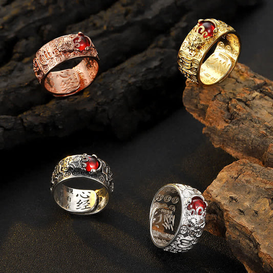 PiXiu Garnet Heart Sutra Ring – Silver lion motif ring with red gemstone cabochon and filigree band held in hand, warm brown rock surface, close-up side angle
