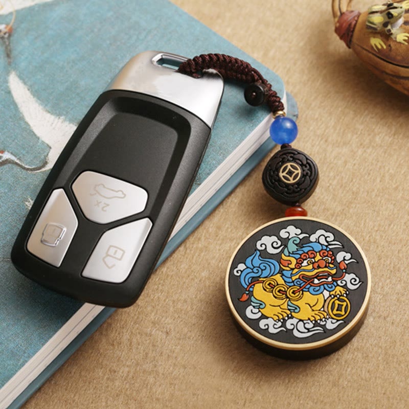 PiXiu Coin Keychain – Attached to car key on blue notebook beside ceramic teapot