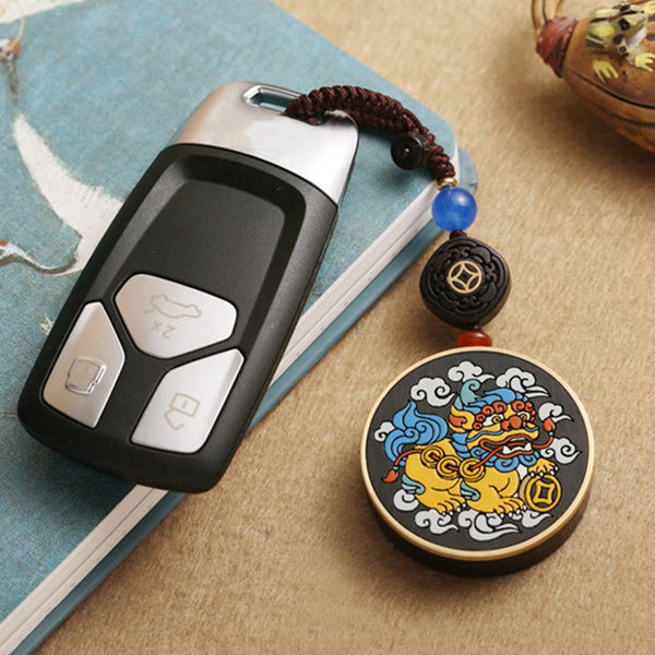 PiXiu Coin Keychain – Attached to car key on blue notebook beside ceramic teapot
