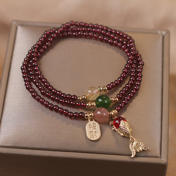 Garnet triple-strand bracelet with koi fish charm red enameled body detailed tail fins and zhao cai wealth attraction gold tag on champagne satin jewelry box presentation