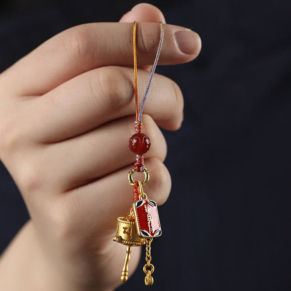 Prayer Wheel Phone Charm – Handheld close-up on dark navy background, spiritual accessory