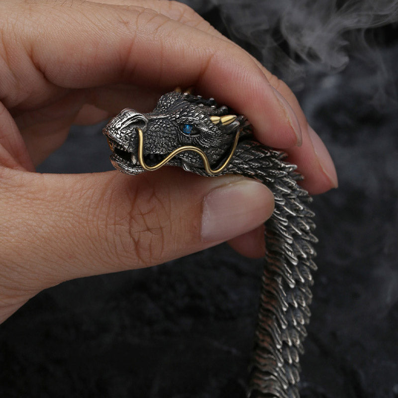 Dragon scale bracelet held in hand showing detailed sculpted dragon head with blue eye gold whiskers and intricately textured overlapping scale body
