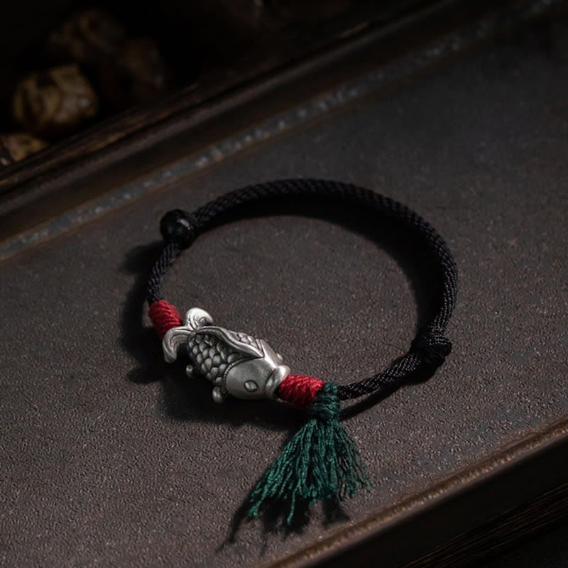925 Sterling Silver Koi Fish Bracelet – silver koi charm on dark wooden tray, red thread wraps and green tassel, moody