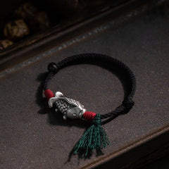 925 Sterling Silver Koi Fish Bracelet – silver koi charm on dark wooden tray, red thread wraps and green tassel, moody