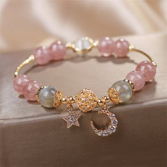 Strawberry Quartz celestial bracelet with translucent pink beads, gray-blue labradorite accents, gold filigree centerpiece, crystal star and moon charms on wood.