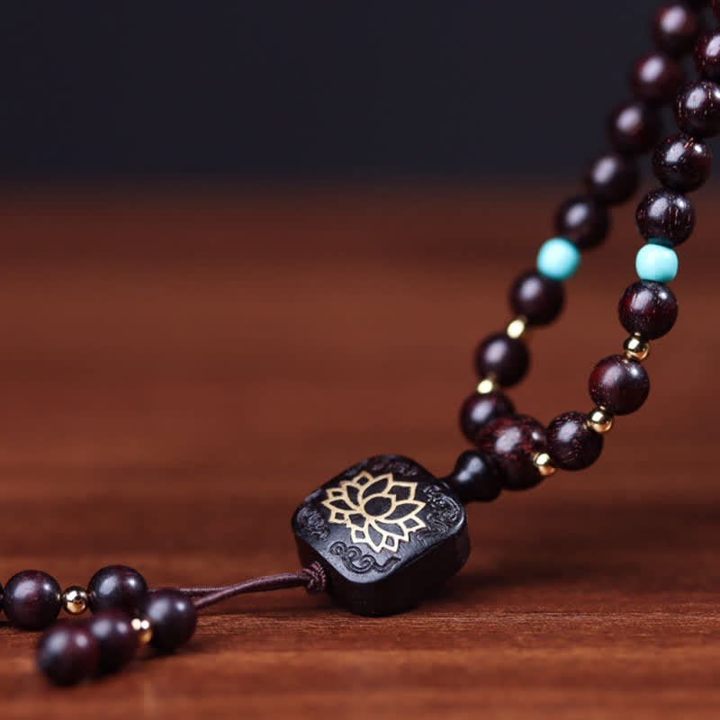 108 bead red sandalwood mala bracelet with turquoise accent beads and gold lotus flower guru bead diagonally arranged on warm wood surface with dark gradient backdrop