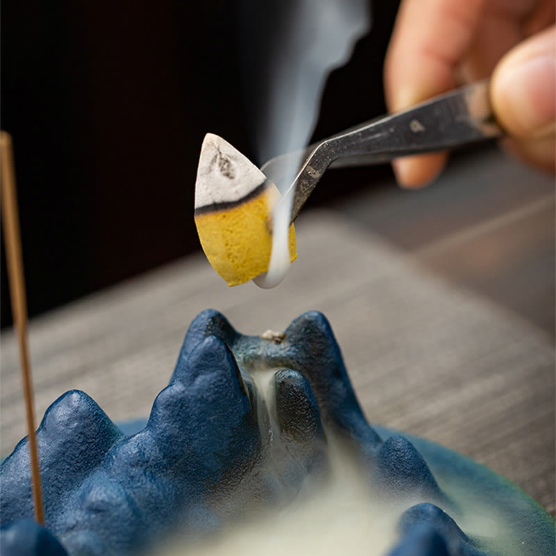 Ceramic Backflow Incense Burner – Cone being placed on blue mountain with tweezers, smoke beginning to flow, zen