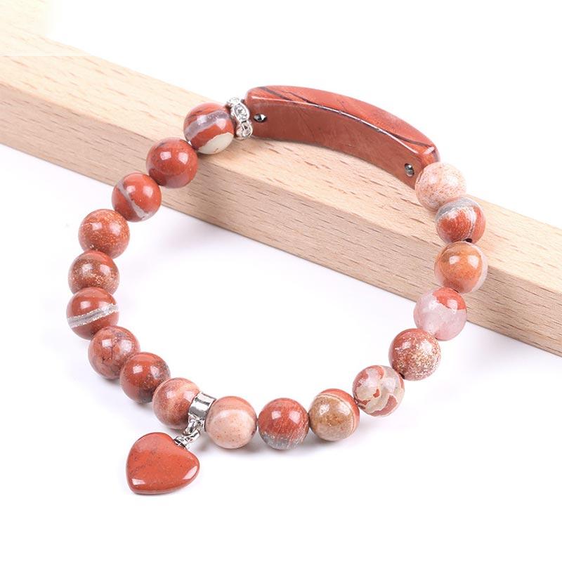 Natural Multi-Stone Love Heart Healing Bracelet - Red jasper bracelet on light wood stand with earthy red-orange beads, natural banding patterns, and heart pendant