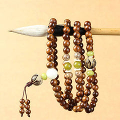 Tibetan Rosewood Bodhi Seed Mala Bracelet hanging on calligraphy brush, showing olive green jade beads and carved bodhi seed accents, white guru bead, traditional 108-bead mala necklace with brown cord tassel