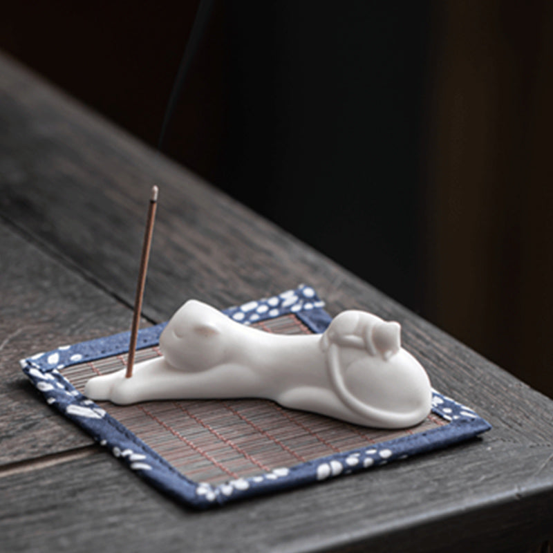 White ceramic cat incense holder with burning stick on blue mat, rustic wood