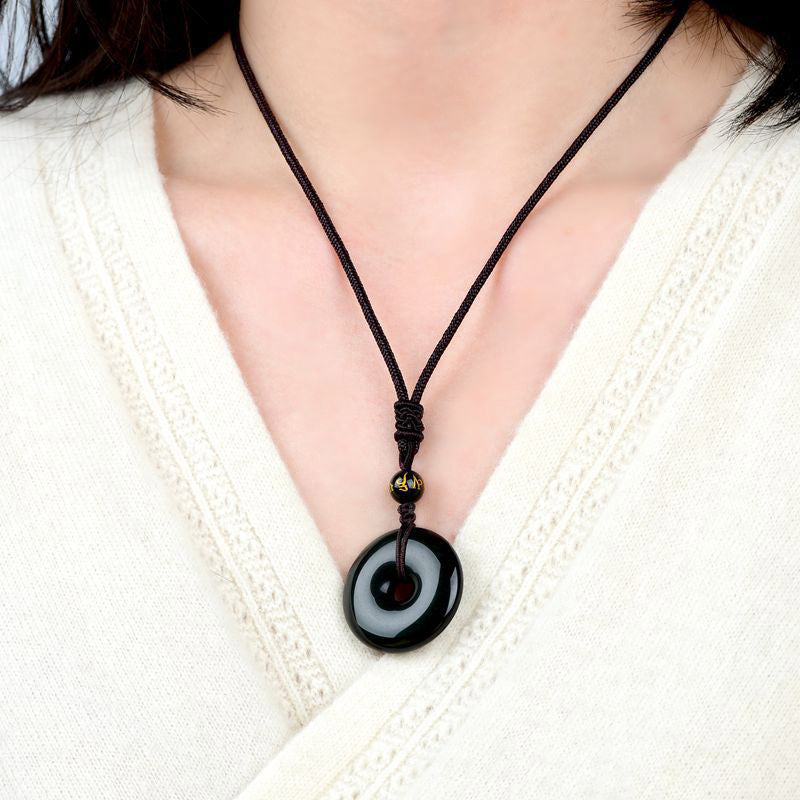Tibetan obsidian protection necklace worn on model showing glossy black bi disc pendant with gold-inscribed mantra bead against cream knit sweater neckline