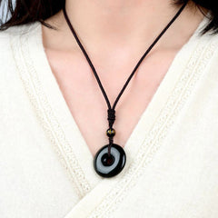 Tibetan obsidian protection necklace worn on model showing glossy black bi disc pendant with gold-inscribed mantra bead against cream knit sweater neckline