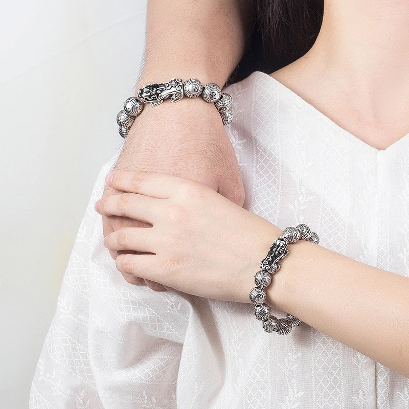 Tibetan Feng Shui PiXiu Silver Bracelet – Worn on crossed wrists showing dual bracelet styling with antique silver Pixiu and Bagua details on white garment