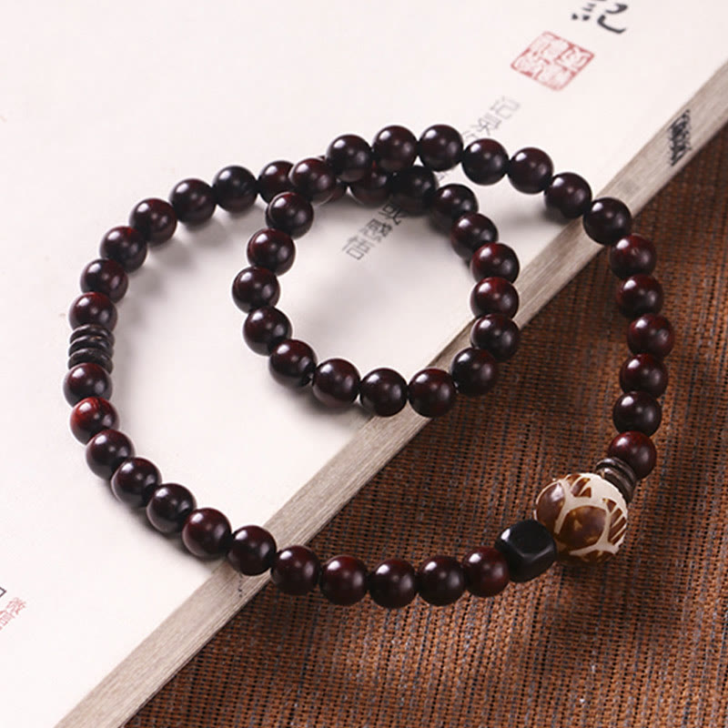 Red Sandalwood Lotus Bodhi Seed Bracelet – Dark wood mala beads with lotus carving on bamboo mat beside calligraphy book