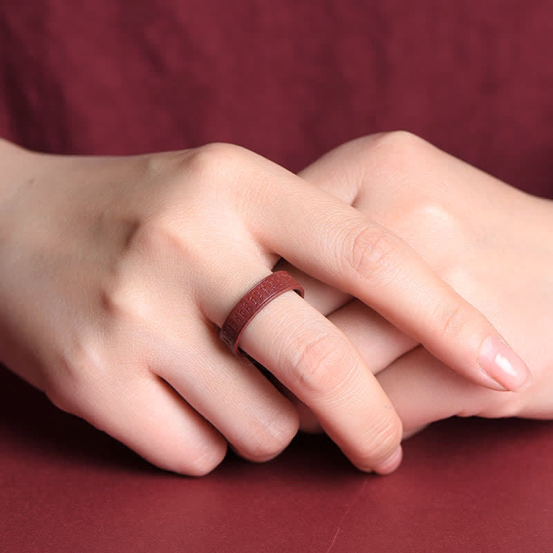 Cinnabar Om Mani Padme Hum Blessing Ring – carved cinnabar ring with relief patterns on clasped hands, burgundy fabric, three-quarter view