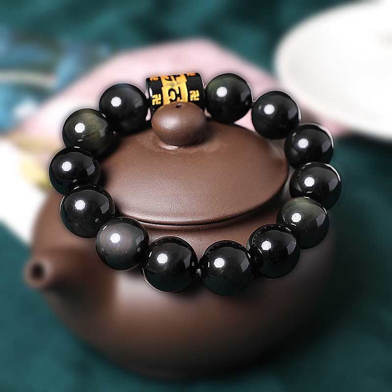 Rainbow Obsidian Bracelet – Black beads with gold mantra bead resting on brown teapot lid, mindfulness bracelet
