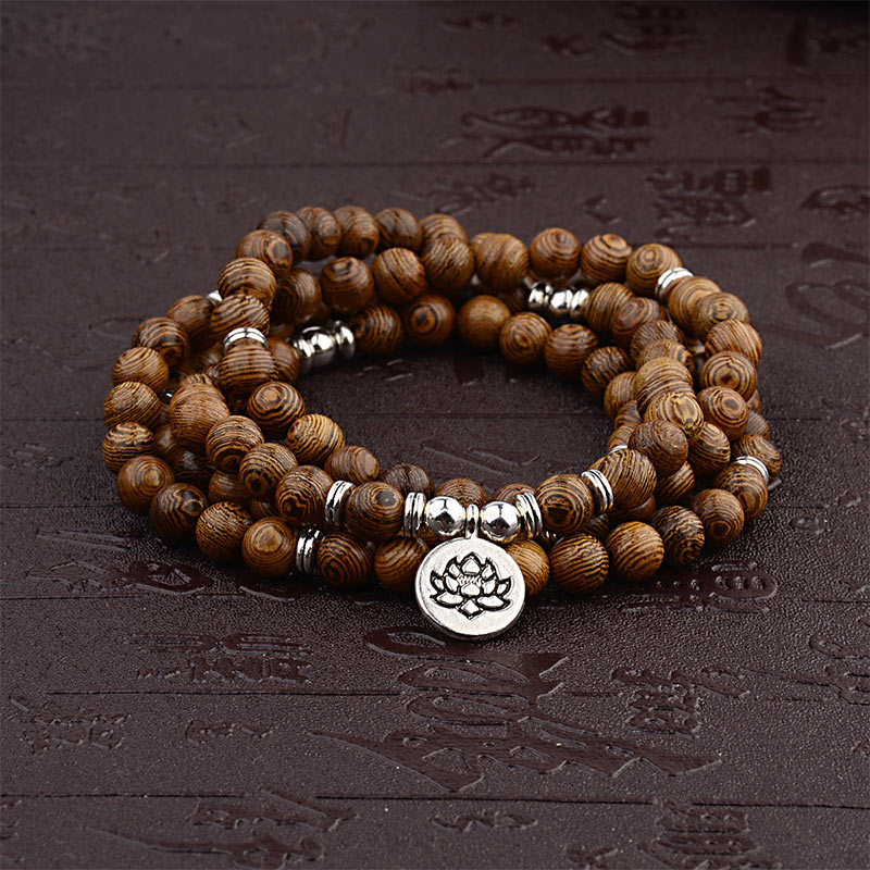 Tibetan Lightning Strike Wood Mala – coiled wrap with lotus charm on dark carved surface, front-view
