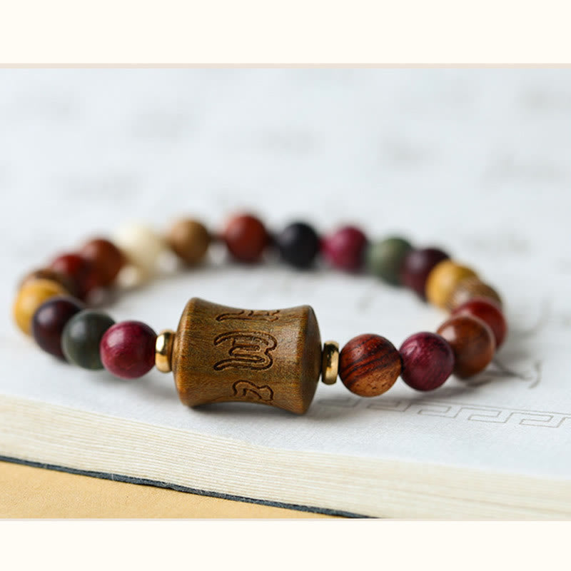 Multicolored Sandalwood Prayer Bracelet – Low angle macro of engraved focal bead on textured page