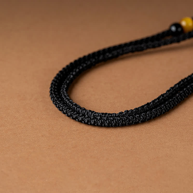 12 Chinese Zodiac Fortune Necklace Pendant – Black braided cord bracelet detail with obsidian bead and golden amber bead, adjustable macrame knot closure, warm tan craft paper background, minimalist unisex healing crystal bracelet