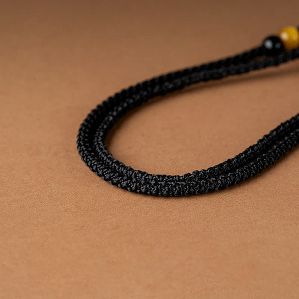 12 Chinese Zodiac Fortune Necklace Pendant – Black braided cord bracelet detail with obsidian bead and golden amber bead, adjustable macrame knot closure, warm tan craft paper background, minimalist unisex healing crystal bracelet