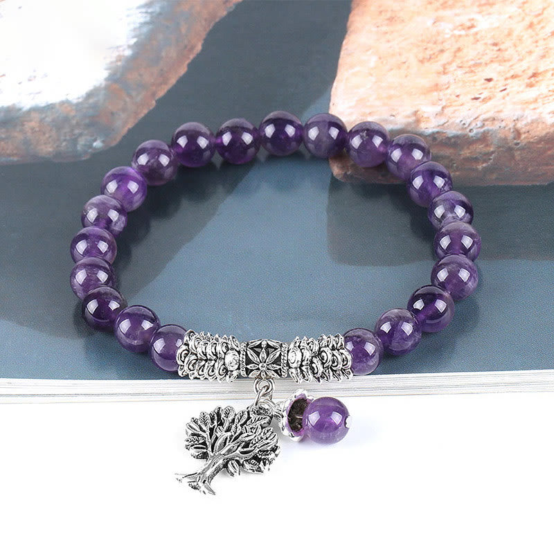 Tree of Life amethyst bracelet with deep purple quartz beads, detailed silver tree charm with leafy canopy and roots, floral spacer bead on gray stone.