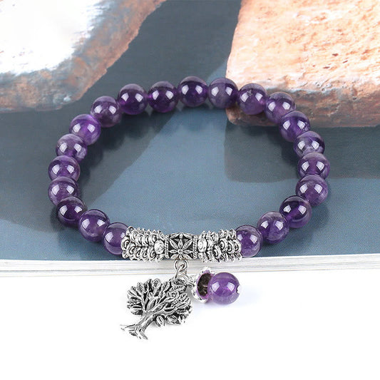 Tree of Life amethyst bracelet with deep purple quartz beads, detailed silver tree charm with leafy canopy and roots, floral spacer bead on gray stone.