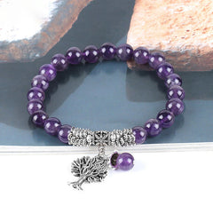 Tree of Life amethyst bracelet with deep purple quartz beads, detailed silver tree charm with leafy canopy and roots, floral spacer bead on gray stone.