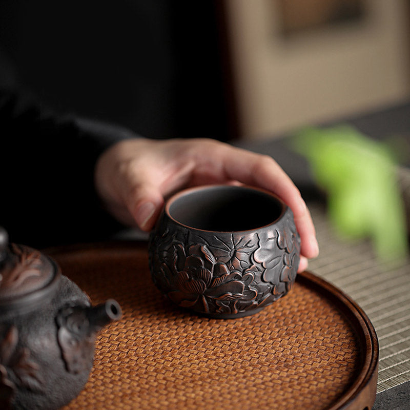 Ceramic Tea Cup – Peony relief carving on dark clay body, studio side view, handcrafted tea bowl