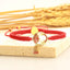 Tibetan Red String Koi Fish Bracelet – red cord on stone with wheat background, gold lotus bird charm and dangles