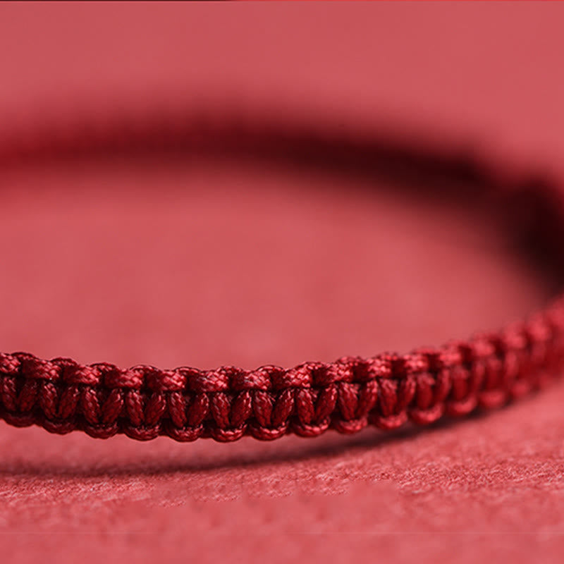 Close-up of dark burgundy braided cord bracelet showing intricate macrame weave pattern on soft pink fabric background