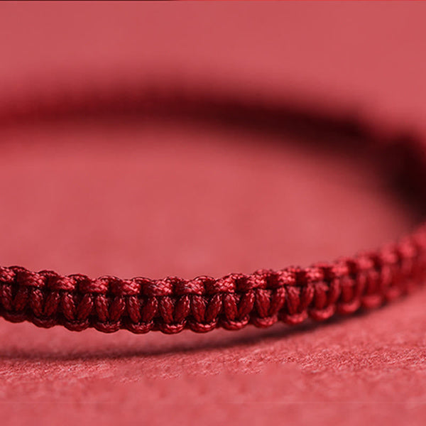 Close-up of dark burgundy braided cord bracelet showing intricate macrame weave pattern on soft pink fabric background