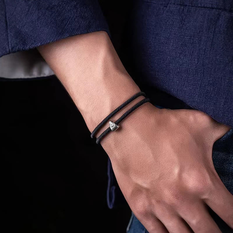 925 Silver Fu Character Braided Bracelet – Black cord bracelet with silver fortune charm worn on wrist against navy blue fabric, lifestyle side view shallow depth