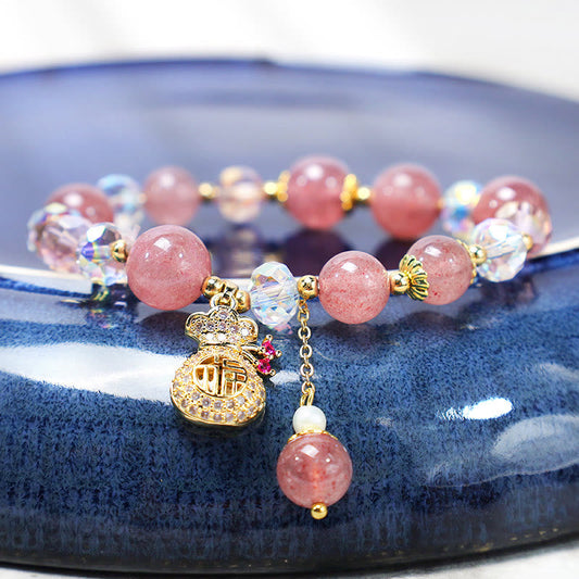 Strawberry quartz beaded charm bracelet with pavé crystal money bag charm featuring Chinese fu fortune character pink crystal AB bead accents and pearl dangle on navy blue ceramic dish display