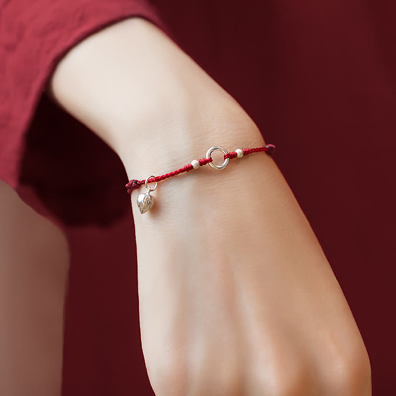 Sterling Silver Lotus Peace Buckle Red String Bracelet – Inner wrist view of the bracelet with silver peace buckle ring, flanking beads, and leaf charm against a burgundy backdrop
