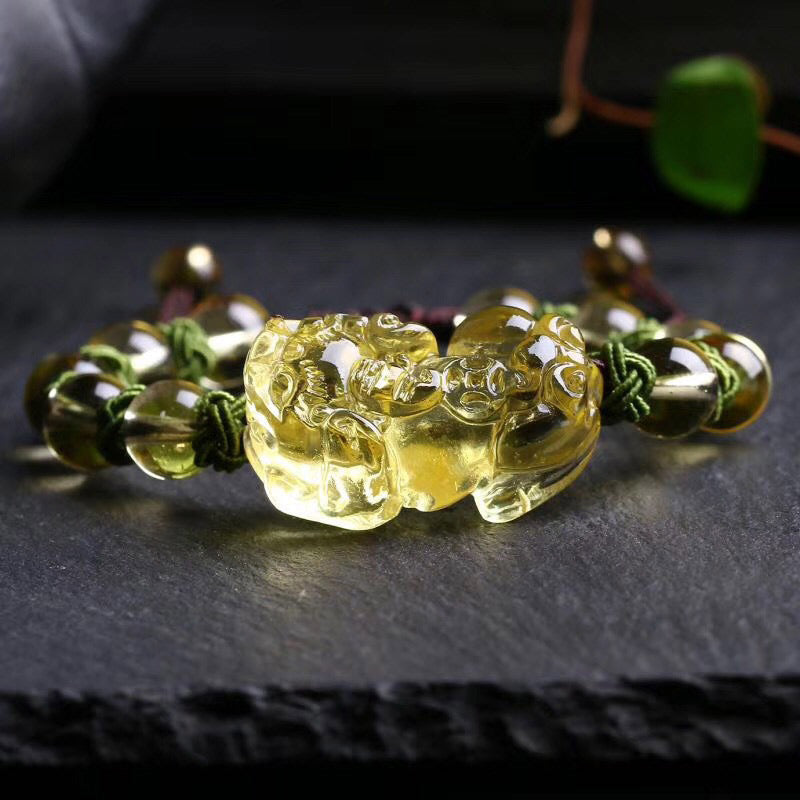 Natural Citrine PiXiu Wealth Bracelet – detailed front view of intricately carved golden citrine PiXiu figure with open mouth wealth symbolism, flanked by polished round citrine beads on green knotted cord, dark background with shallow depth of field