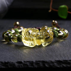 Natural Citrine PiXiu Wealth Bracelet – detailed front view of intricately carved golden citrine PiXiu figure with open mouth wealth symbolism, flanked by polished round citrine beads on green knotted cord, dark background with shallow depth of field