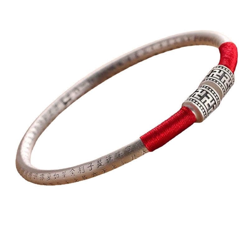 Tibetan Red String Bracelet – overhead view on white, silver bangle with engraved text and red cord
