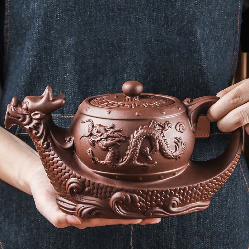 Vintage Dragon Auspicious Clouds Teapot – reddish-brown dragon teapot held by hand on denim, authentic artisan scale