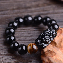 Obsidian Tiger Eye PiXiu Bracelet close-up on weathered wood, carved mythical beast detail, protective amulet
