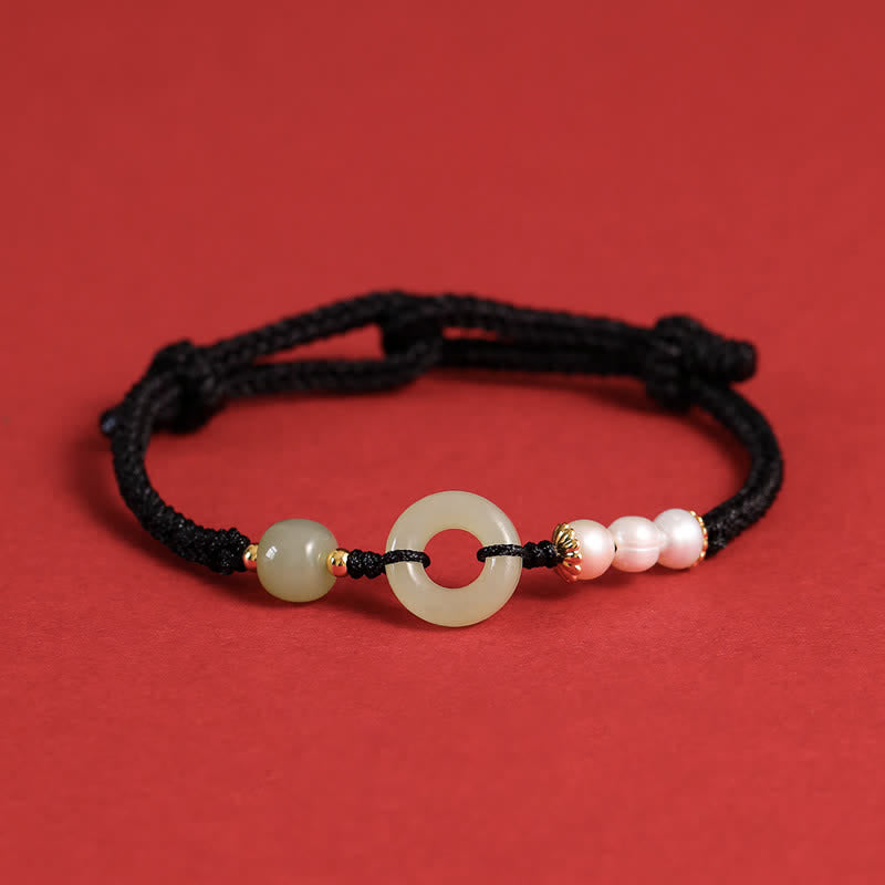 Hetian Jade Pearl Peace Buckle Bracelet – black braided cord with jade disc and pink pearls, gold caps, red background frontal view