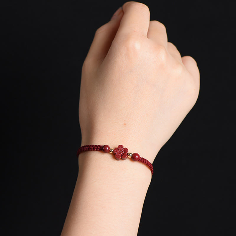 Burgundy braided cord bracelet with carved five-petal flower charm and gold spacer beads worn on wrist against solid black background