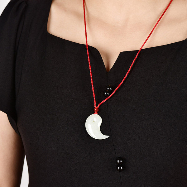 Yin Yang Jade Necklace – Pale green jade crescent pendant on red cord with carnelian bead, brown background
