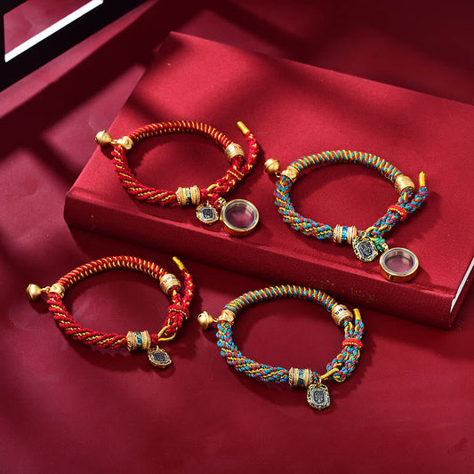 Zakiram Goddess Wealth Bracelet – Two braided cord bracelets in red-gold and blue-green-yellow with gold charms on deep red velvet surface
