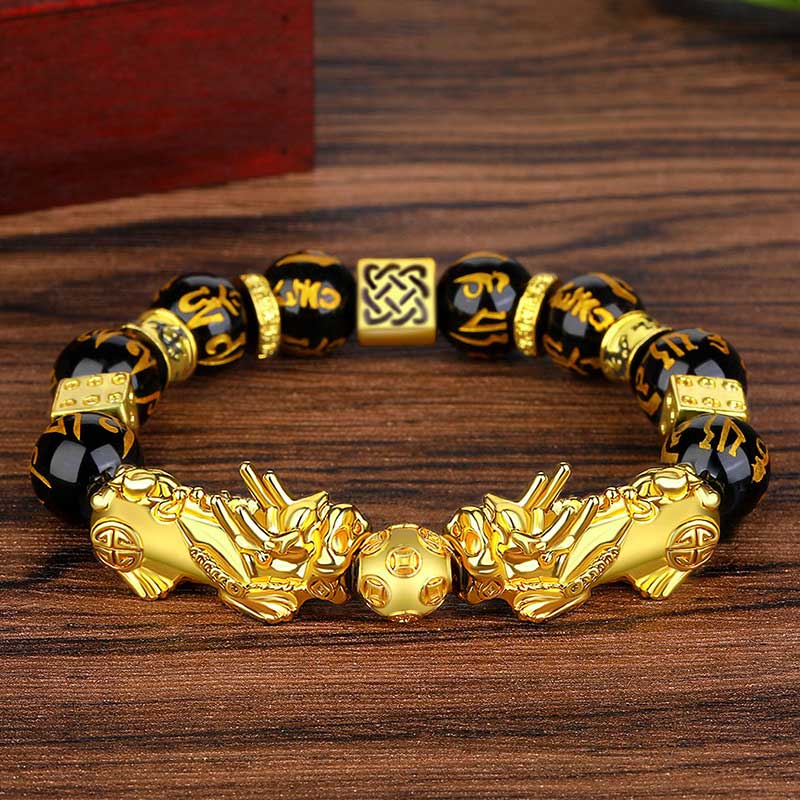 Double Pixiu Obsidian Bracelet – laid on warm wood surface with obsidian mantra beads, Pixiu wealth charm